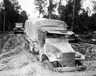 A black-and-white photo of a World War II truck driving through deep mud. This was the kind of terrain the truckers often faced. The truck has a collapsible hood and a canvas-covered flatbed with supplies.