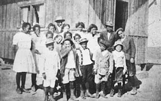 The black-and-whte photograph shows a group of about 20 people--mostly children--dressed up for their photograph. The girls are mostly wearing white. Some of the boys have casual jackets on.