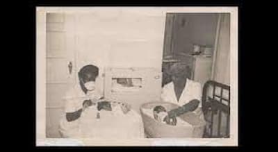 This is a black-and-white photograph of two midwives taking care of two infants.