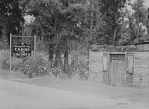 A sign that advertises "Cabins for Colored." The area around it is in poor condition but we don't see the cabins