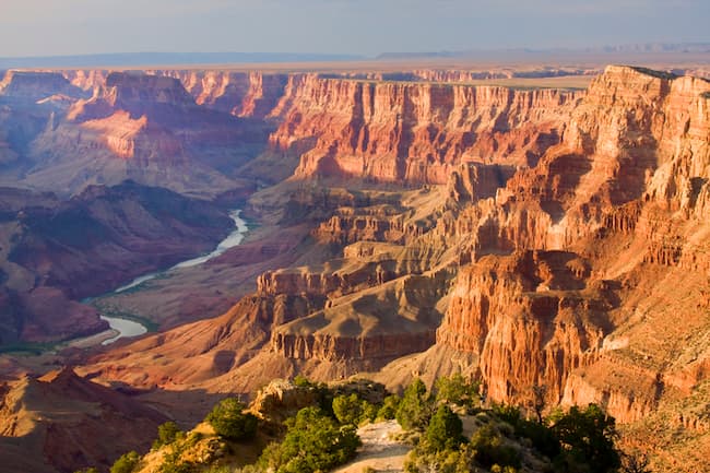 a beautiful view of the Grand Canyon from the South rim. The river is visble, as are many levels of cliffs. The colors range from dark to lighter red.