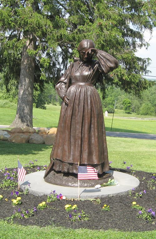 This is a current color photo of the statue of Elizabeth. She is obviously pregnant and wear an apron. Her right hand touches her enlarged belly protectively. Her left hand is wiping her brow in the July heat.