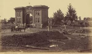 This is a contemporary black-and-white photo that shows the Evergreen gatehouse, mae of brick. Two buildings are on either side of the arch to give lining space for those who care for the cemetery.