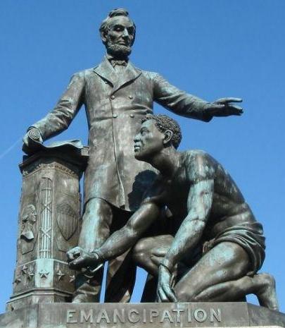Abraham Lincoln stands above a chained Black man who is dressed only in a loin cloth. 