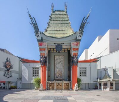This is a color photograph showing the distinctive roofline of the TCL Chinese Theater on Hollywood Blvd. The roof is green and appears to be thatched. The columns in front are bright orange.