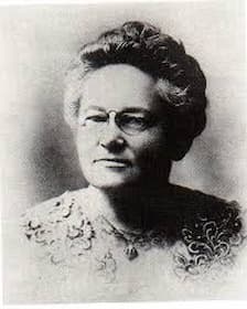 A black and white photo of an older Fannie Farmer, posing for a headshot. She wears a lace dress and a necklace.
