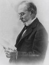 A black and white photo of Dr. Carlos Finlay. The photo is a profile view and he hold papers in his hands that he is studying.