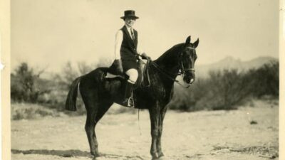 Ina Gittings mounted on horseback wearing jodhpurs and a hat