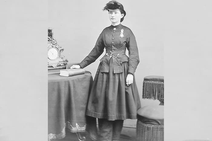 Mary Walker is dressed in a fancy jacket and skirt and wear a hat with a feather. She prominently wears her Medal of Honor over her heart.