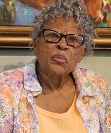A color photograph depicting Ola Lee in a flowered shirt and glasses--grey curly hair.