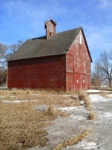Red barn with cupola. Field is partially covered in snow.