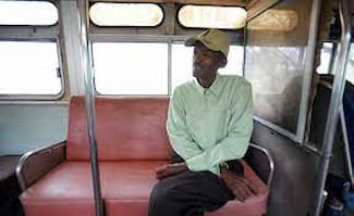 This is a color photograph of Crawford sitting alone inside one of the buses that he used for his business.