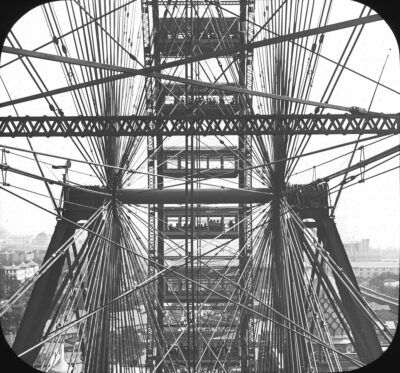 This is a black-and-white photo from within the BigWheel. People are riding in at least two of the cabins, the the steel girders and the web of work to make the ride function is very clear.