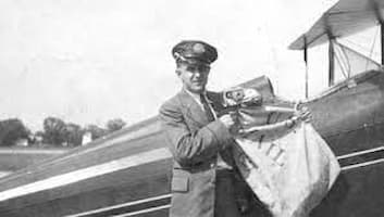 postal worker standing by biplane, either picking up the mail or dropping it off.