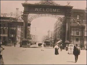 This is a grainy black and white photo of a Denver street showing the Welcome Arch built for the Democrats arriving for the convention. You can see a woman in a full-length skirt (it was 1908) and men in suits wearing hats.