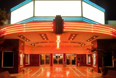 In a color photo from the street, this picture shows the Art Deco lighting design and the grand but welcoming presentation of a movie palace theater.