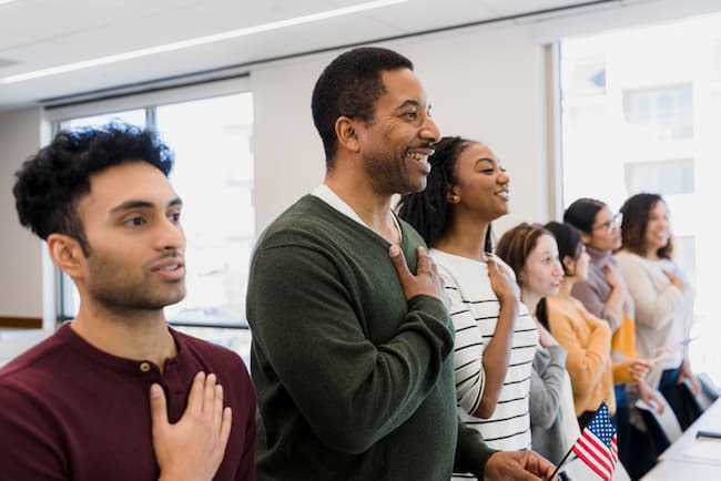 A multicultural group of new citizens saying the Pledge of Allegiance with their hands over their hearts.
