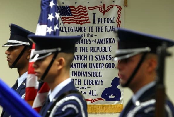 Soldiers are at attention servomg as a color guard. Behinkd them is a poster of the Pledge of Allegiance. istock images
