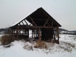 Barn with many slats missing. It is clearly disintegrating. Snow is on the ground.