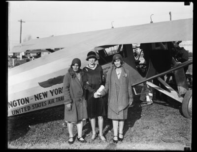 women standing by early airplane 1928